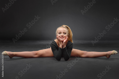 beautiful white caucasian girl gymnast doing gymnastic exercise for flexibility and stretching on black background.