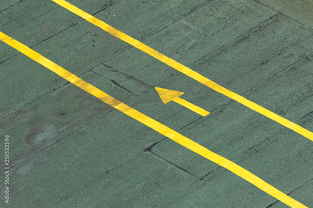 Directional traffic yellow arrow on a green tarmac texture floor. Directional traffic yellow arrow on a green tarmac texture floor.