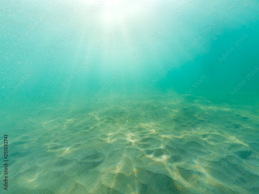 Underwater blue sea background. Underwater view of ocean, sand and sun lights.
