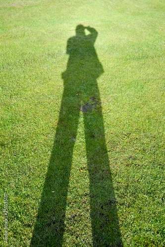 Shadow of a man on a background of green grass illustrates the concept of a photographer.