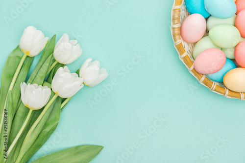top view of white tulips and easter eggs in wicker plate isolated on blue