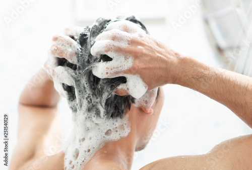 Closeup young man washing hair with with shampoo in the bathroom, health care concept