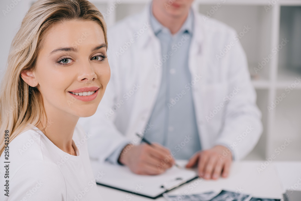 selective focus of beautiful woman looking at camera during consultation with male dentist in clinic