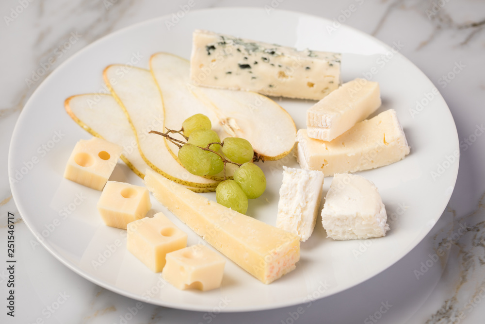 Käseteller mit Edamer, Parmesan, Blauschimmel Käse und Ziegenkäse an Birne und Trauben auf Teller und Marmor Hintergrund