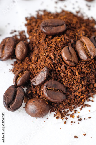 Close up dark roasted coffee beans and coffee ground on white cotton fabric and white filter paper background in natural light 