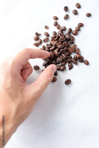 person s hand picking up dark roasted coffee beans on white cotton fabric background in natural light 