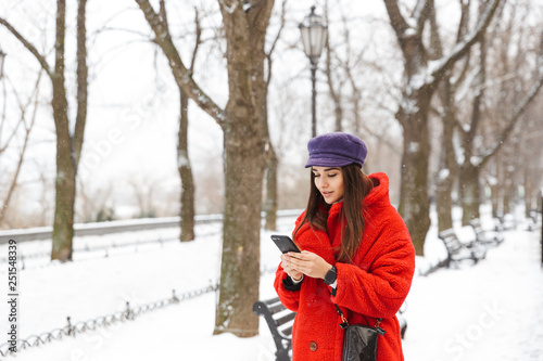 Beautiful young woman using mobile phone walking outdoors in snow winter.
