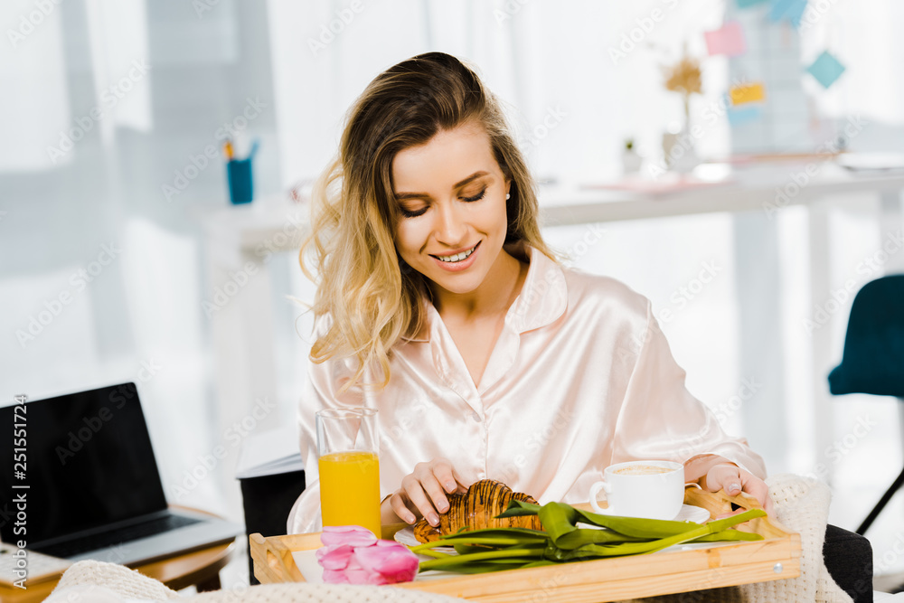 Young woman in satin pyjamas eating breakfast with smile Young woman in satin pyjamas eating breakfast with smile