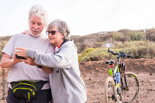 Adult mature caucasian couple smile and enjoy the outdoor sport activity with mountain bikes while check maps and paths on cellulaer internet connected phone - technology and healthy lifestyle