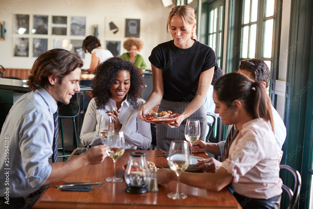 Waitress Serving Meal To Business Colleagues Sitting Around Restaurant Table