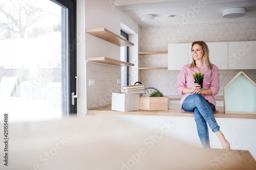A young woman moving in new home, sitting on a counter in the kitchen.