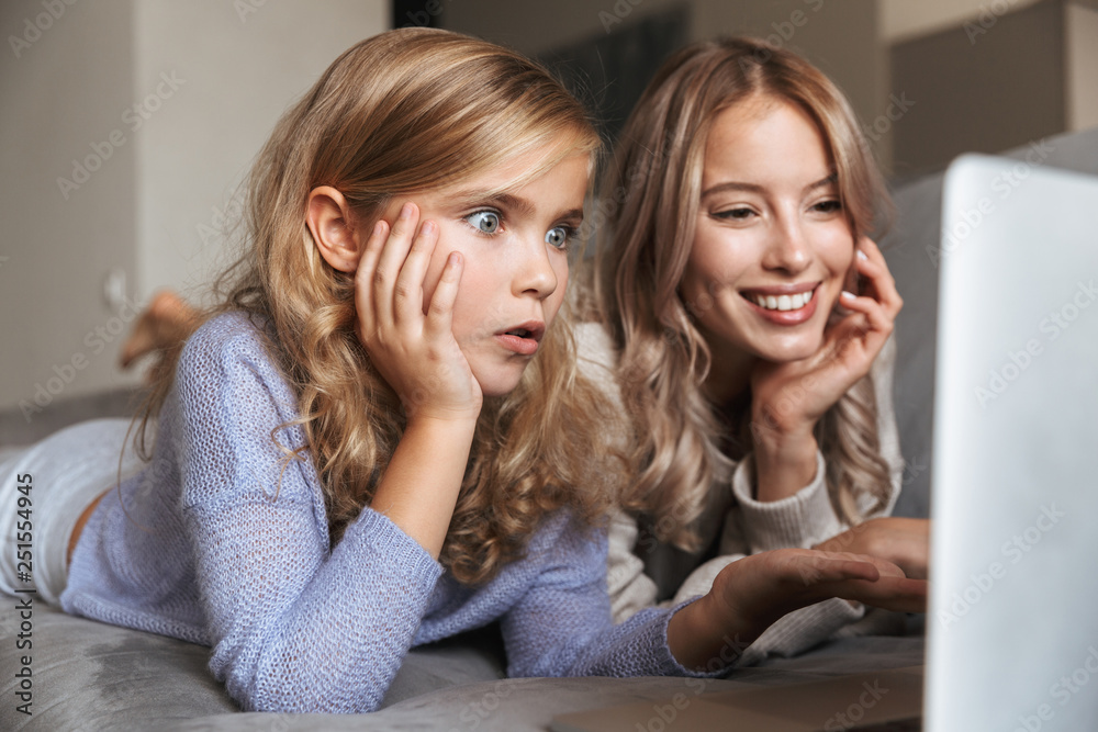 Young woman with her little sister indoors at home using laptop computer. Young woman with her little sister indoors at home using laptop computer.