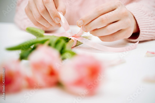 Young woman tying a ribbon on a bouquet of pink tulips.