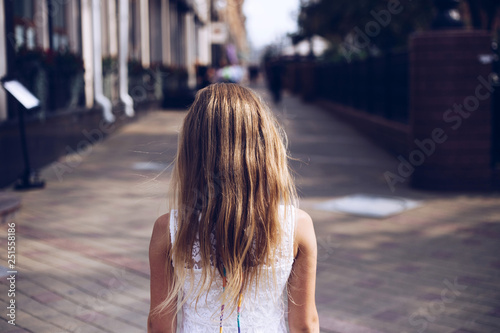 A girl teenager in white dress standing back on the street of the city.