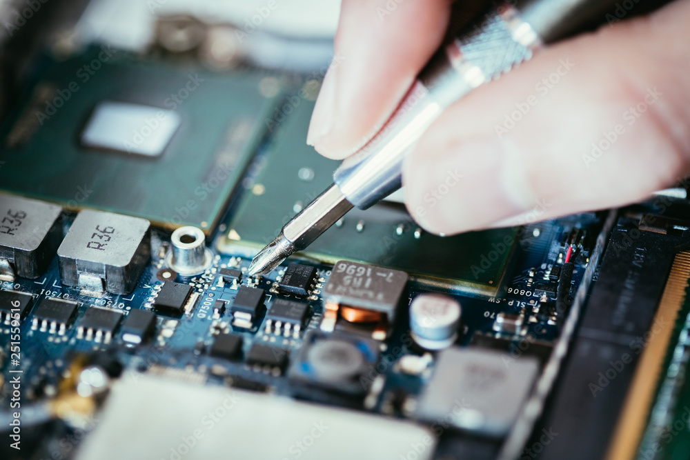 Technician is fixing a computer circuit board, hand and screwdriver.