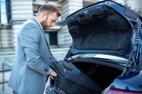 Classy man placing the luggage in the trunk of the car