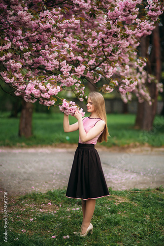 Attractive girl in dress stand in park by the blossom tree. Blond hair female