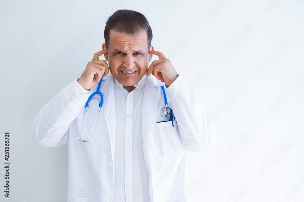 Middle age doctor man wearing stethoscope and medical coat over white background covering ears with fingers with annoyed expression for the noise of loud music. Deaf concept. Middle age doctor man wearing stethoscope and medical coat over white background covering ears with fingers with annoyed expression for the noise of loud music. Deaf concept.