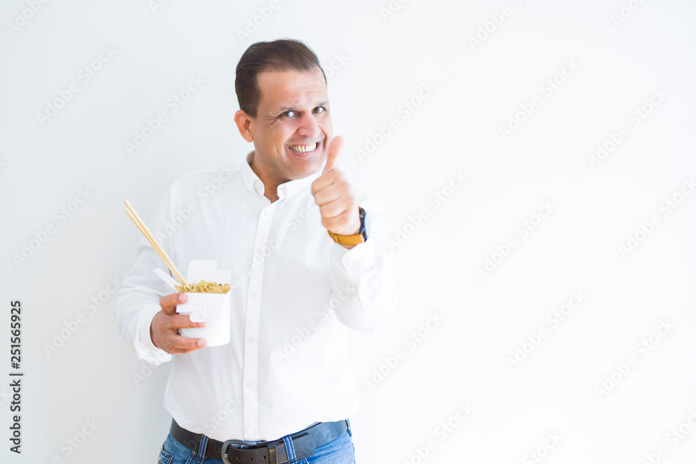 Middle age man eating asian noodles from take away carton happy with big smile doing ok sign, thumb up with fingers, excellent sign Middle age man eating asian noodles from take away carton happy with big smile doing ok sign, thumb up with fingers, excellent sign