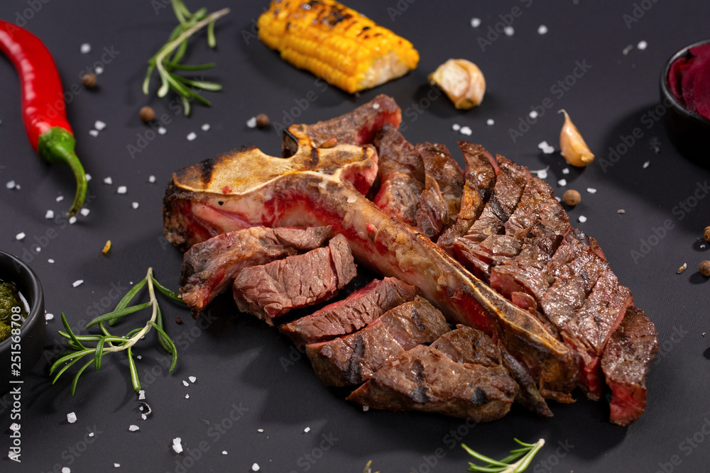 Medium rare grilled Steak Ribeye Black Angus with corn and rosemary on serving on black background
