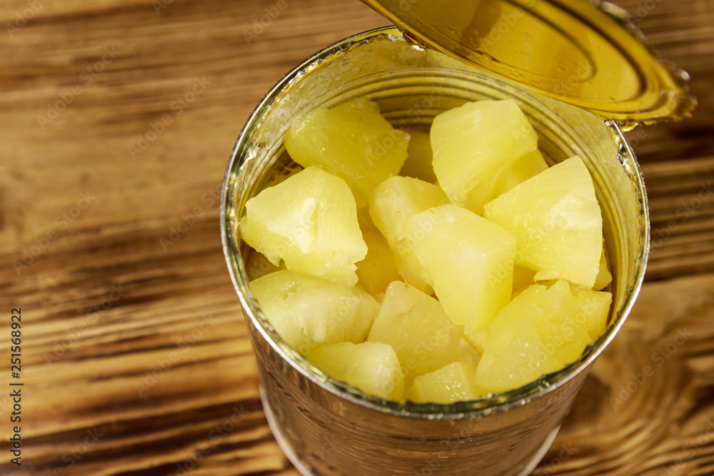 Opened tin can of pineapple pieces on wooden table Opened tin can of pineapple pieces on wooden table