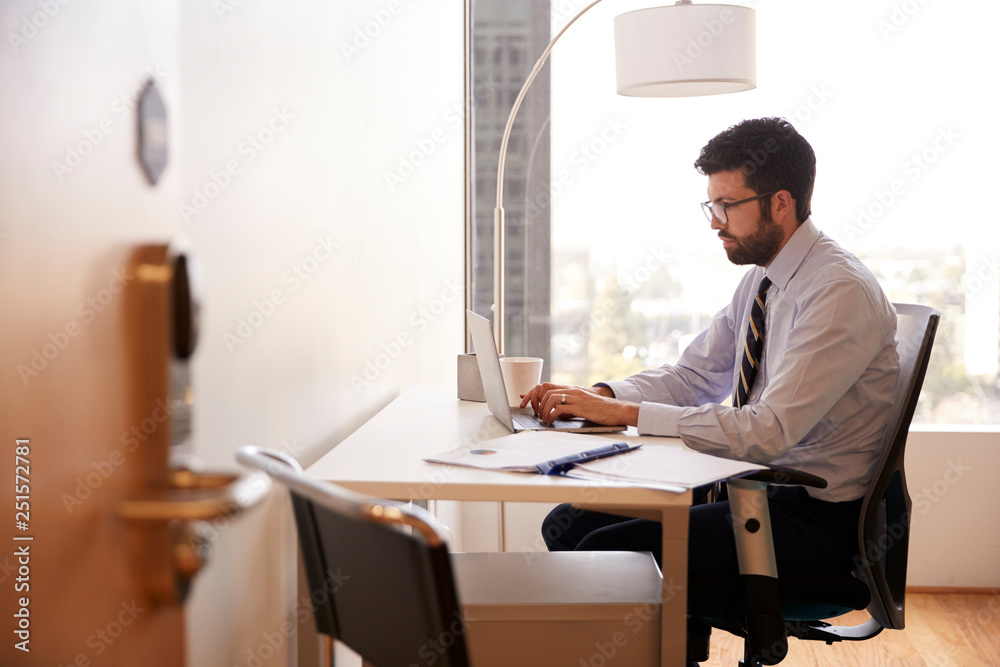 Businessman Sitting At Desk Working On Laptop In Modern Office
