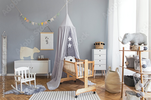 Stylish and bright scandinavian decor of  newborn baby room with mock up poster, white design furnitures, natural toys, hanging grey canopy with wooden cradle, bookstand, accessories and teddy bears.  photo