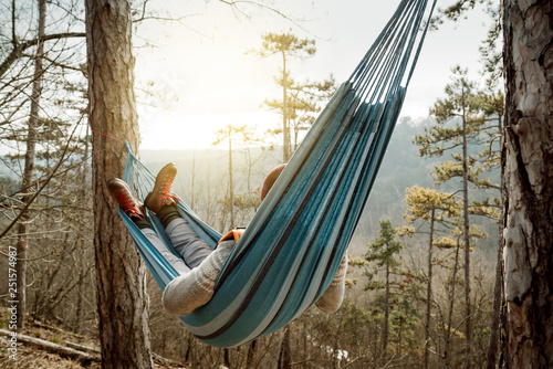Young happy man relaxing lying in hammock on top of mountain.