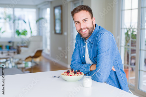Handsome man having breakfast eating cereals at home and smiling