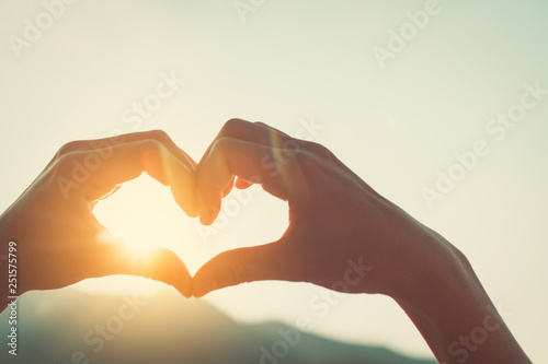Female hands heart shape at top of mountain on sunset sky abstract background.