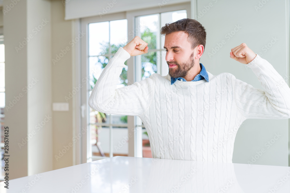 Handsome man wearing casual sweater showing arms muscles smiling proud. Fitness concept.