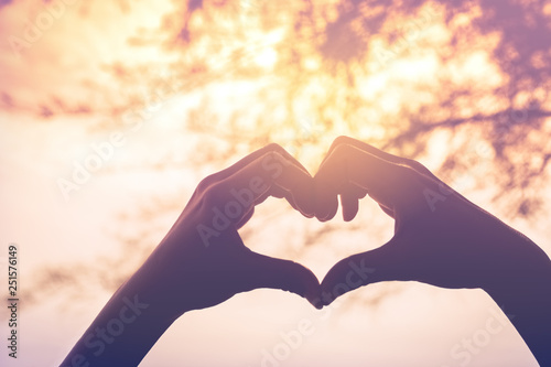 Female hands heart shape on nature bokeh sun light flare and blur leaf abstract background.