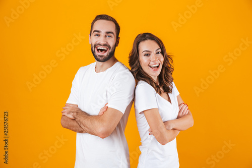Image of young people man and woman in basic clothing smiling, while standing together isolated over yellow background