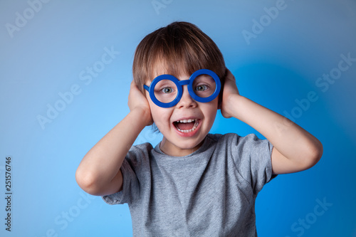 Portrait of a beautiful cute baby boy in blue glasses on a blue background.