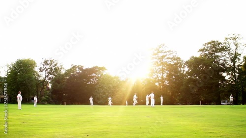 English cricket, bowler bowls to batter. Sunset in background.