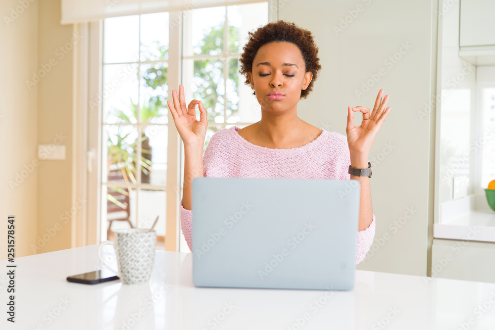 Young african american woman working using computer laptop relax and smiling with eyes closed doing meditation gesture with fingers. Yoga concept. Young african american woman working using computer laptop relax and smiling with eyes closed doing meditation gesture with fingers. Yoga concept.
