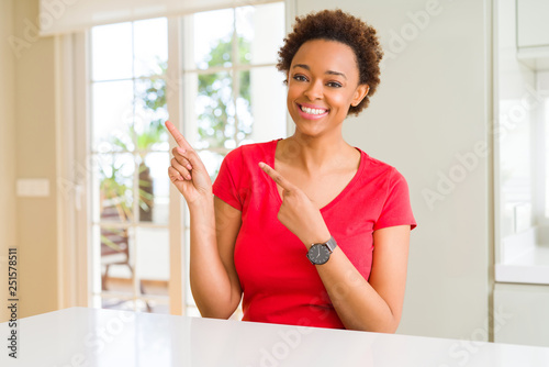 Young beautiful african american woman at home smiling and looking at the camera pointing with two hands and fingers to the side.