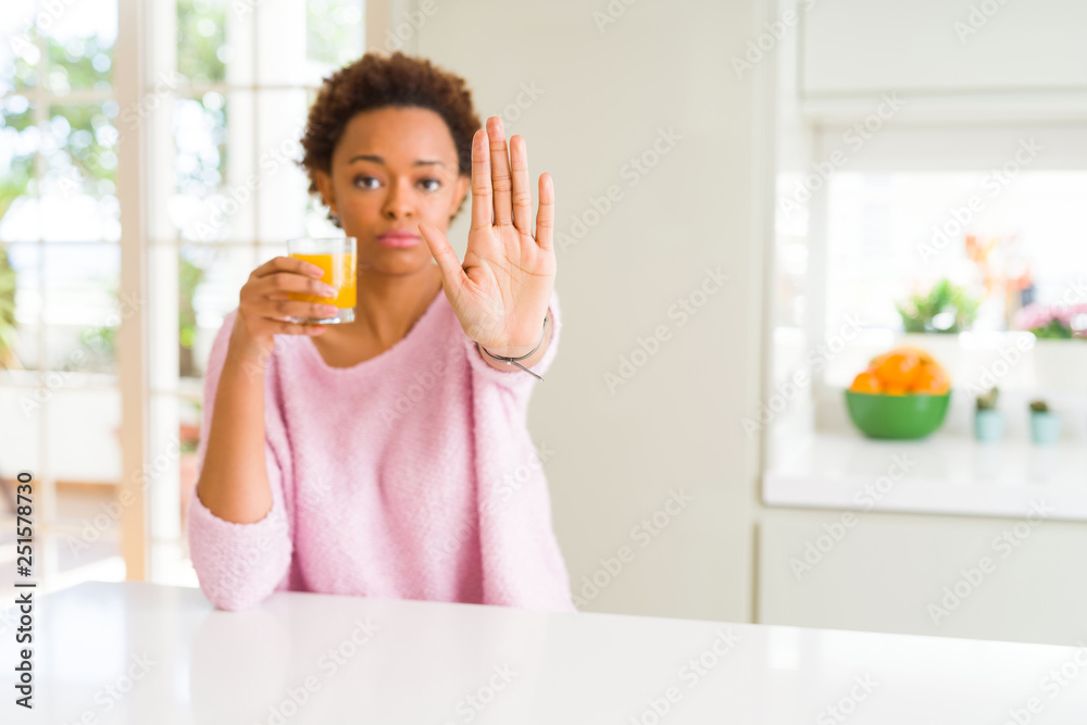 Young african american woman driking orange juice at home with open hand doing stop sign with serious and confident expression, defense gesture Young african american woman driking orange juice at home with open hand doing stop sign with serious and confident expression, defense gesture