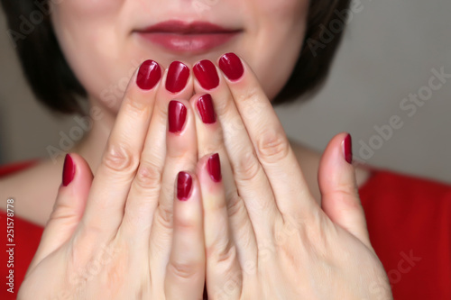 Manicure and makeup, female cosmetics, beauty shop. Perfect hands with red nail polish, part of smiling woman's face with red lips