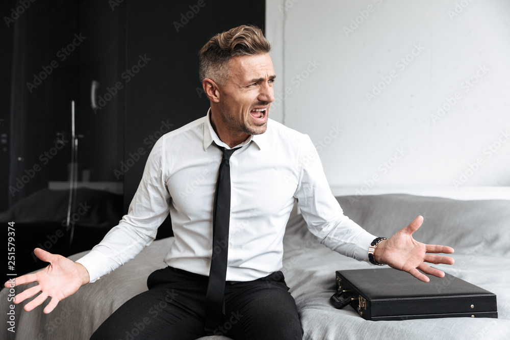 Screaming emotional business man in bedroom indoors at home sitting on bed. Screaming emotional business man in bedroom indoors at home sitting on bed.