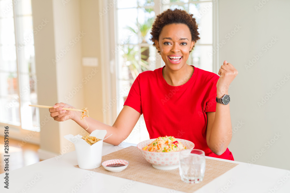 Young african american woman with afro hair eating asian food at home screaming proud and celebrating victory and success very excited, cheering emotion Young african american woman with afro hair eating asian food at home screaming proud and celebrating victory and success very excited, cheering emotion