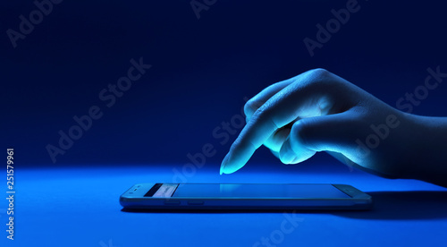 Female hand touching the screen of phone in dark blue environment photo