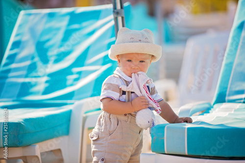 Stylish little baby boy, playing on the beach with plush comforting toy and hat