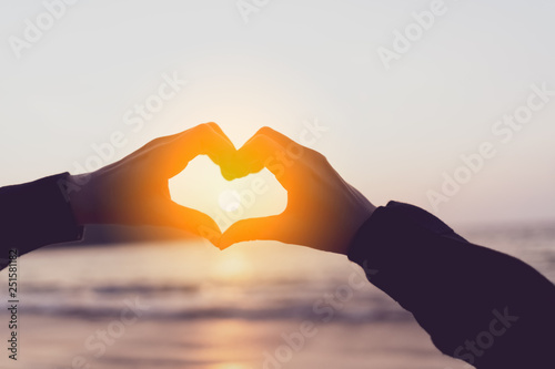 Female hands heart shape on nature bokeh sun light flare wave and blur tropical beach abstract background.