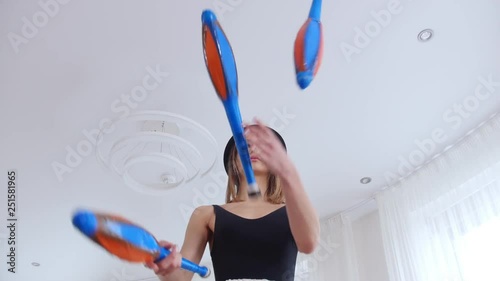 Young woman in a black hat and wearing glasses juggling in bright studio