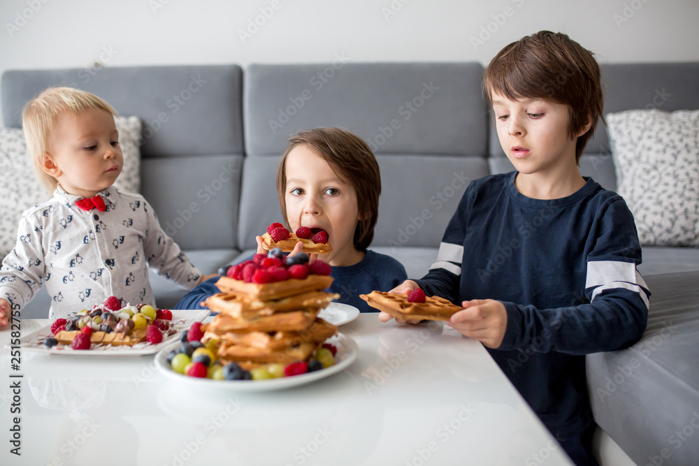 Sweet toddler birthday boy and his brothers, eating belgian waffle with raspberries, blueberries, cocnut and chocolate for breakfast Sweet toddler birthday boy and his brothers, eating belgian waffle with raspberries, blueberries, cocnut and chocolate for breakfast