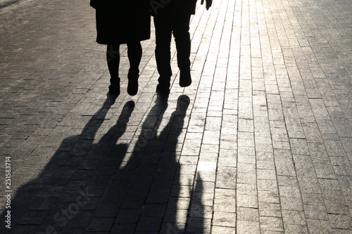 Couple walking down the street, black silhouettes and shadows of two people on pedestrian sidewalk. Male and female legs, concept of relationships, city life, dramatic stories