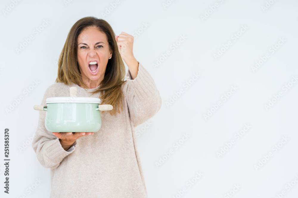 Middle age housewife woman holding iron cooking pot over isolated background annoyed and frustrated shouting with anger, crazy and yelling with raised hand, anger concept Middle age housewife woman holding iron cooking pot over isolated background annoyed and frustrated shouting with anger, crazy and yelling with raised hand, anger concept