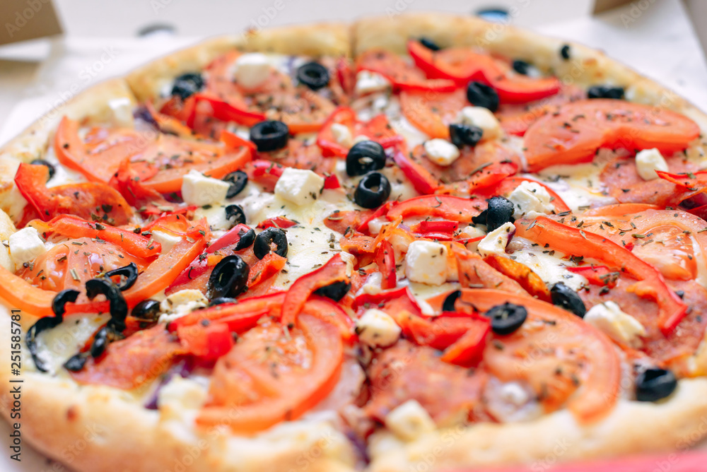 One Greek pizza in a cardboard box on a light background. The view from the top. Pizza delivery. Pizza menu. Pizza on the kitchen table. One Greek pizza in a cardboard box on a light background. The view from the top. Pizza delivery. Pizza menu. Pizza on the kitchen table.