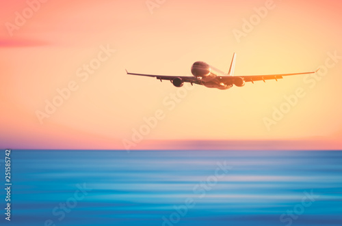 Airplane flying over blur tropical beach with smooth wave and sunset sky abstract background. © tonktiti